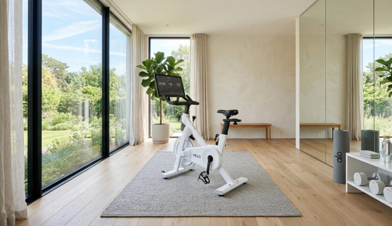 Minimalist home gym featuring a sleek white stationary bike on high-end wooden floors with large mirrors, reflecting an overseas interior design style.